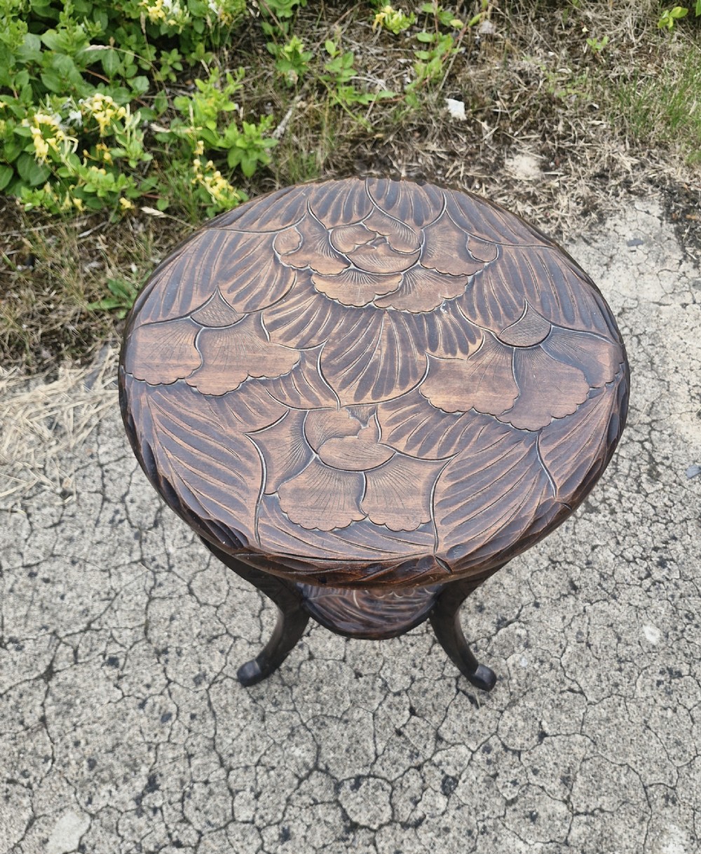 A dark brown carved wood two-tier occasional table with floral leaf carvings on the circular top and lower shelf, supported by four curved legs. View IV