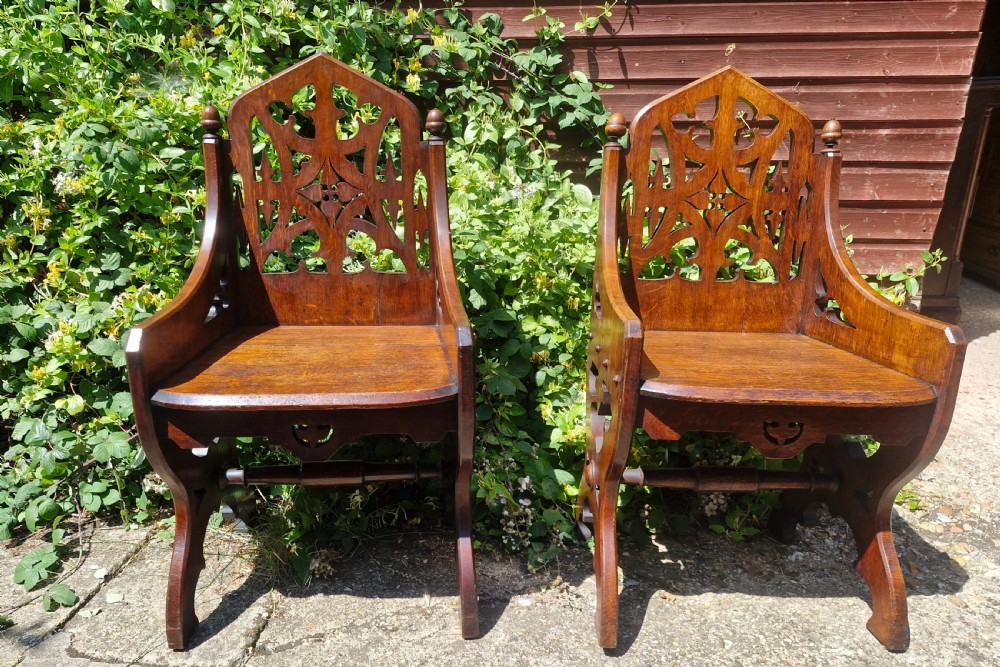 A pair of Victorian Gothic oak hall chairs featuring pierced tracery backrests, pointed arches, small finials, and solid oak seats.