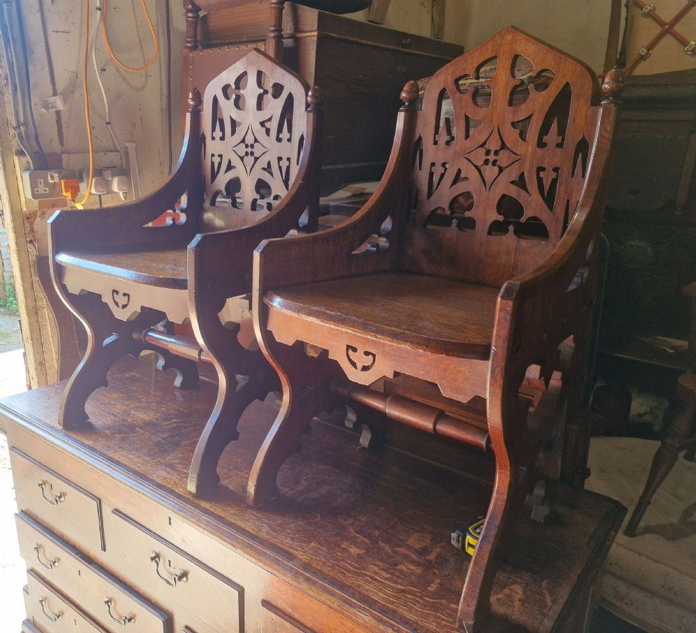 A pair of Victorian Gothic oak hall chairs featuring pierced tracery backrests, pointed arches, small finials, and solid oak seats. View II