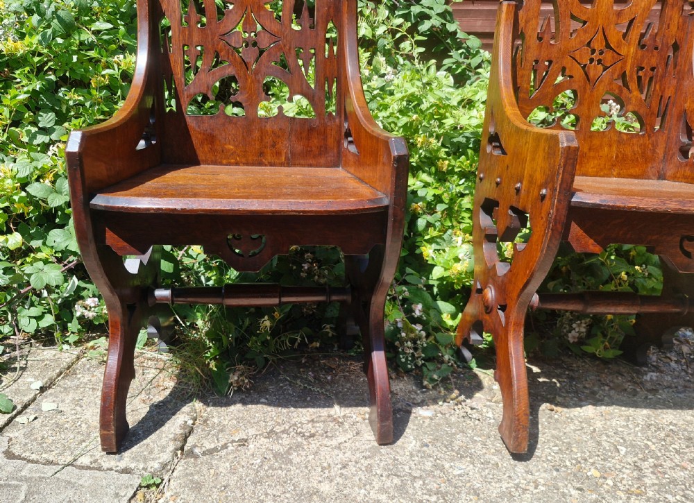 A pair of Victorian Gothic oak hall chairs featuring pierced tracery backrests, pointed arches, small finials, and solid oak seats. View III