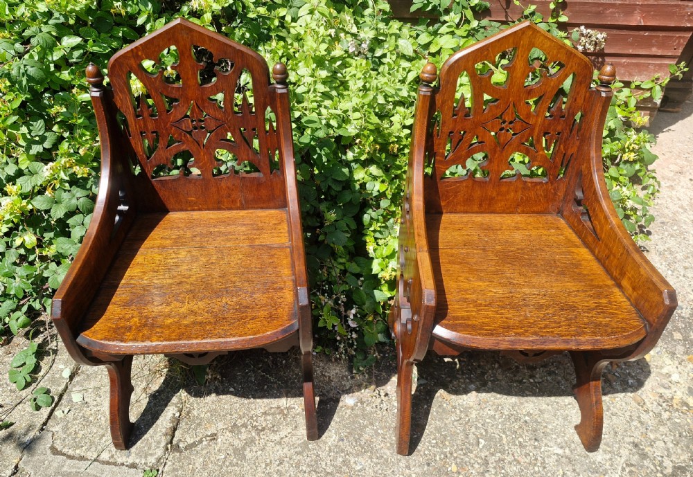 A pair of Victorian Gothic oak hall chairs featuring pierced tracery backrests, pointed arches, small finials, and solid oak seats. View IV