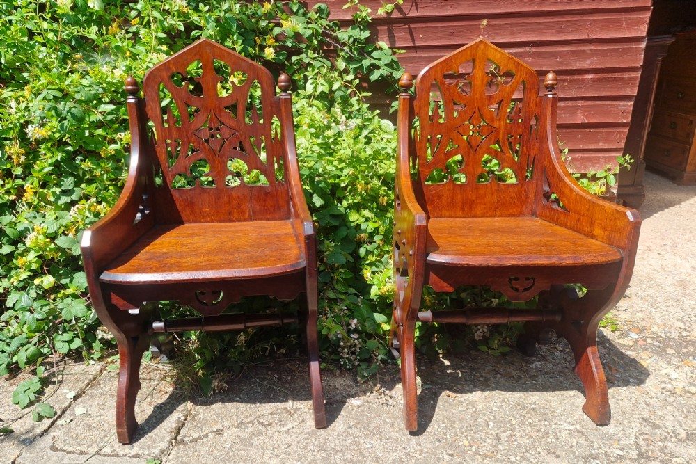 A pair of Victorian Gothic oak hall chairs featuring pierced tracery backrests, pointed arches, small finials, and solid oak seats. View VII