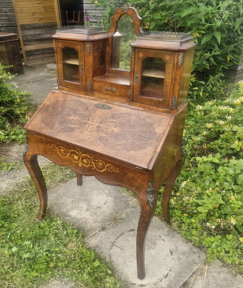 A Victorian burr walnut bonheur du jour writing desk featuring floral marquetry inlay, cabriole legs, a slant front slope, and a mirrored upper superstructure with glazed cabinets.