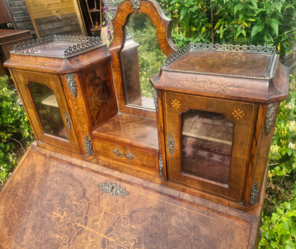 A Victorian burr walnut bonheur du jour writing desk featuring floral marquetry inlay, cabriole legs, a slant front slope, and a mirrored upper superstructure with glazed cabinets. View II