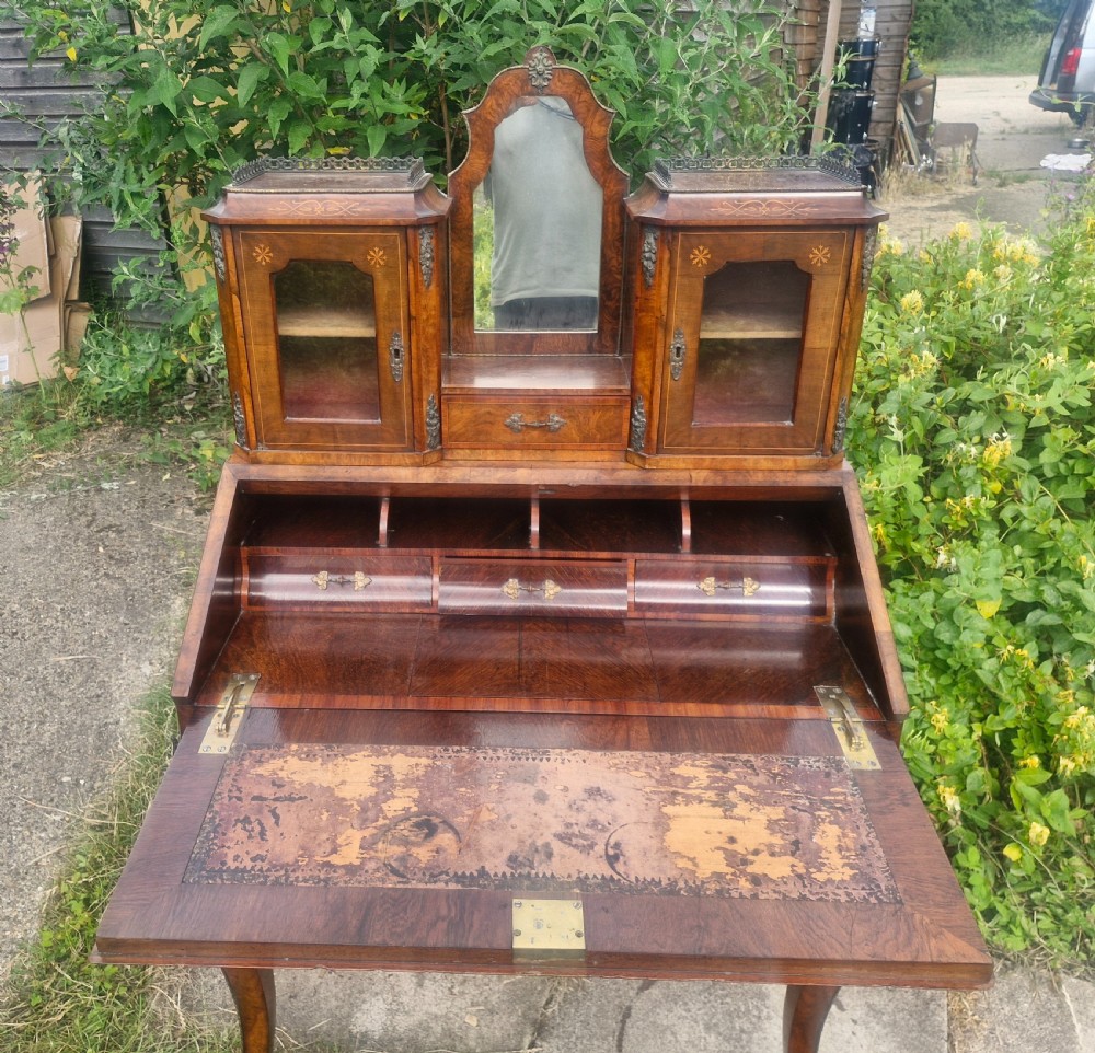 A Victorian burr walnut bonheur du jour writing desk featuring floral marquetry inlay, cabriole legs, a slant front slope, and a mirrored upper superstructure with glazed cabinets. View IV
