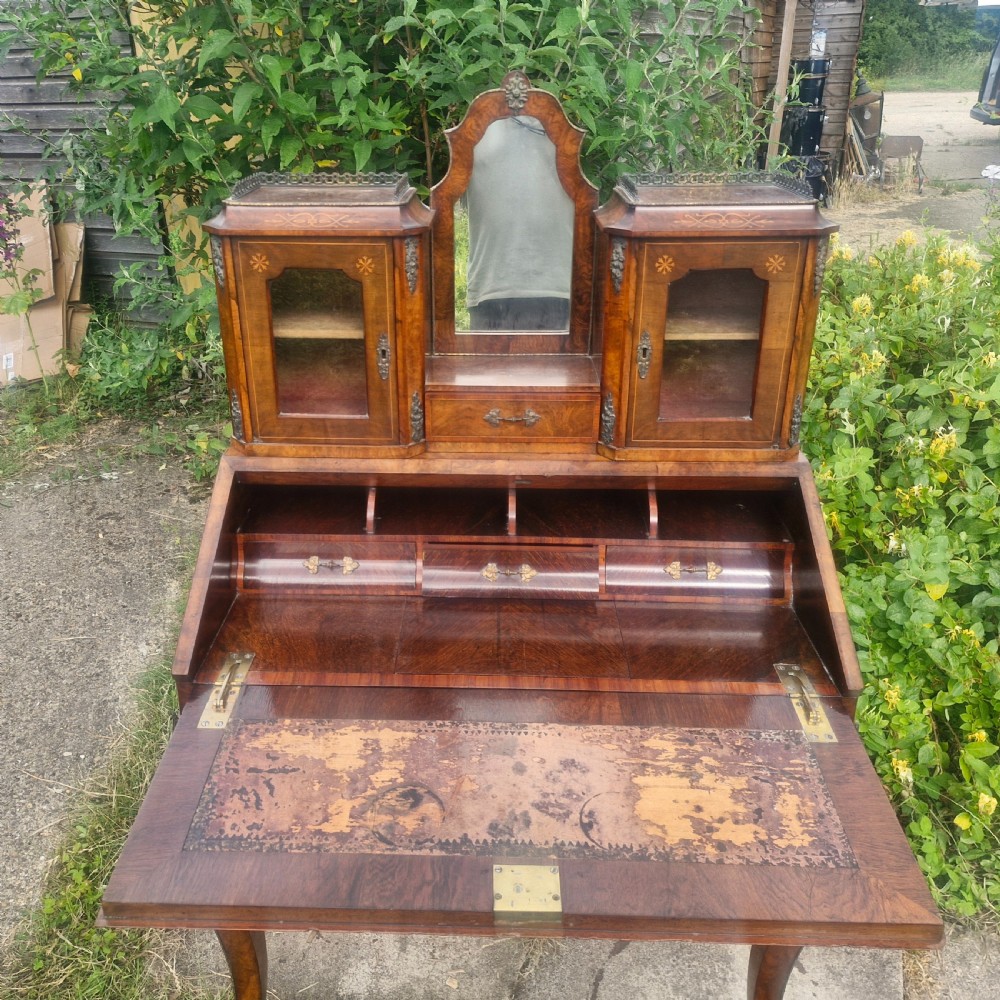 A Victorian burr walnut bonheur du jour writing desk featuring floral marquetry inlay, cabriole legs, a slant front slope, and a mirrored upper superstructure with glazed cabinets. View V