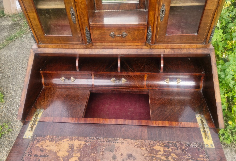 A Victorian burr walnut bonheur du jour writing desk featuring floral marquetry inlay, cabriole legs, a slant front slope, and a mirrored upper superstructure with glazed cabinets. View VI