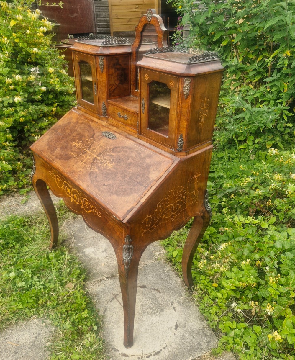 A Victorian burr walnut bonheur du jour writing desk featuring floral marquetry inlay, cabriole legs, a slant front slope, and a mirrored upper superstructure with glazed cabinets. View VII