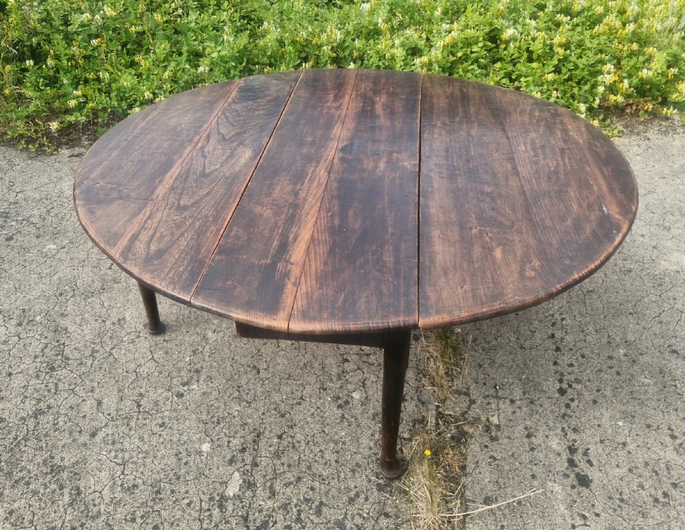 A dark brown circular Georgian country dining table made of elm wood planks supported by four turned legs.