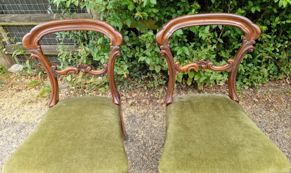 A pair of early Victorian rosewood balloon back side chairs featuring carved foliate splats, cabriole front legs, and green velvet upholstered seats. View V