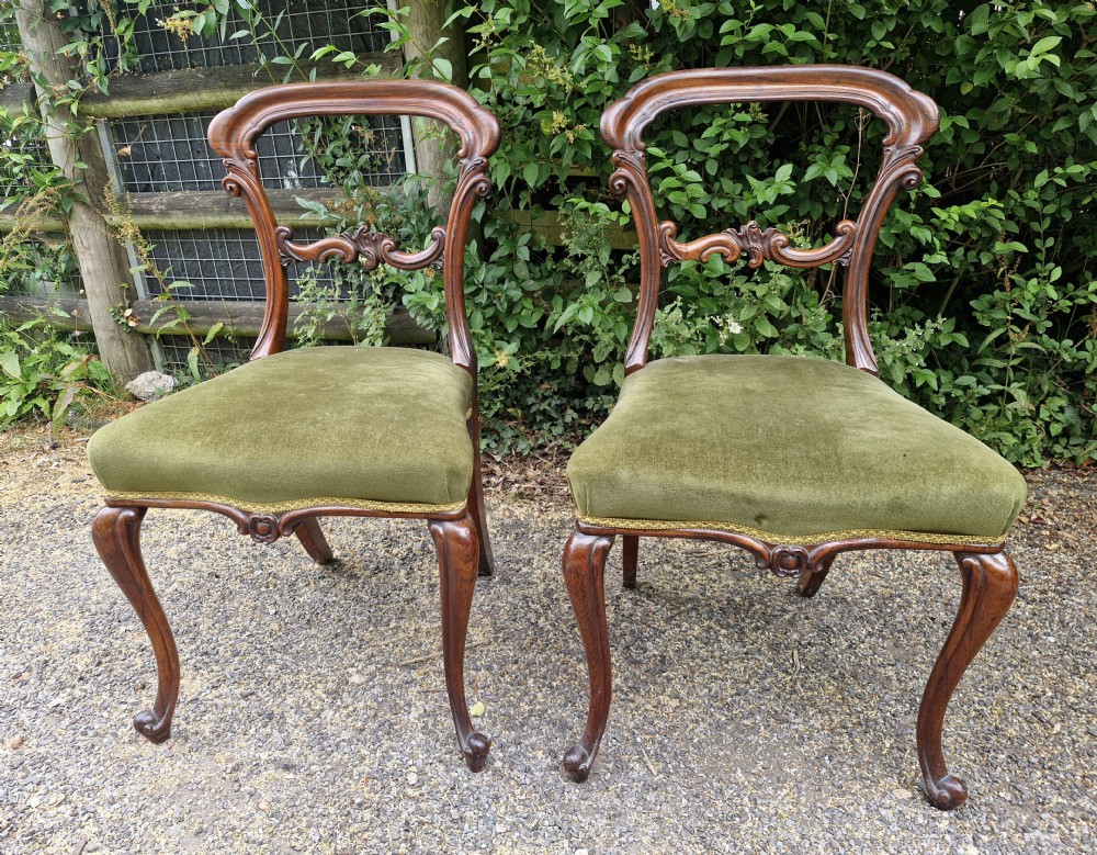 A pair of early Victorian rosewood balloon back side chairs featuring carved foliate splats, cabriole front legs, and green velvet upholstered seats. View VI