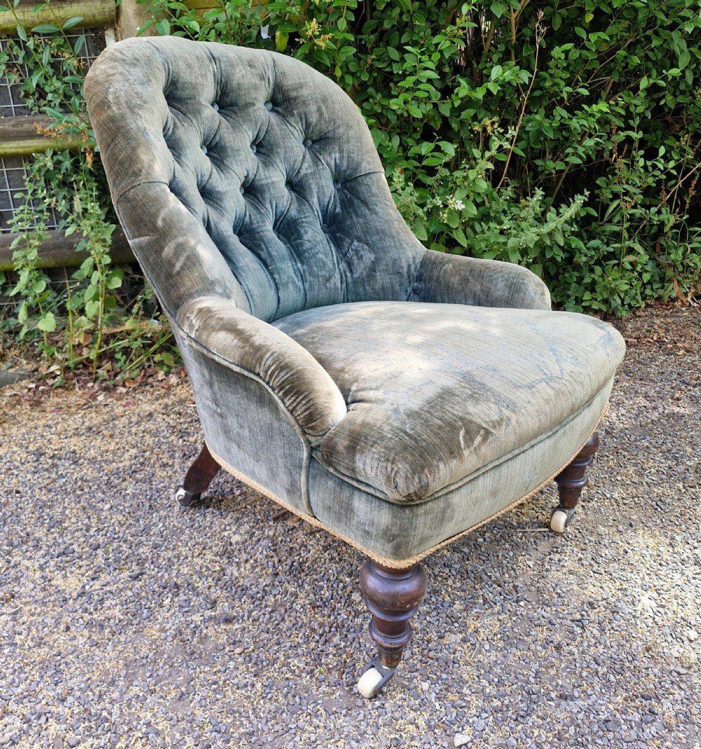 A Victorian button-back armchair upholstered in slate blue velvet featuring turned wooden front legs on castors.