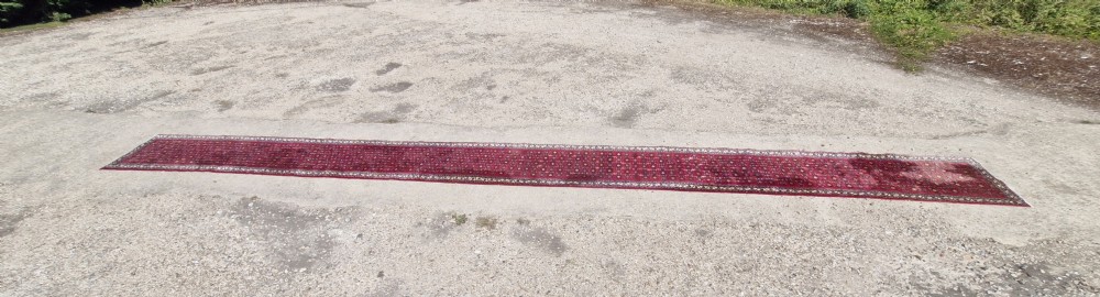An extra long hand-knotted carpet runner displaying a red ground with geometric medallion patterns and detailed side borders. View XIII