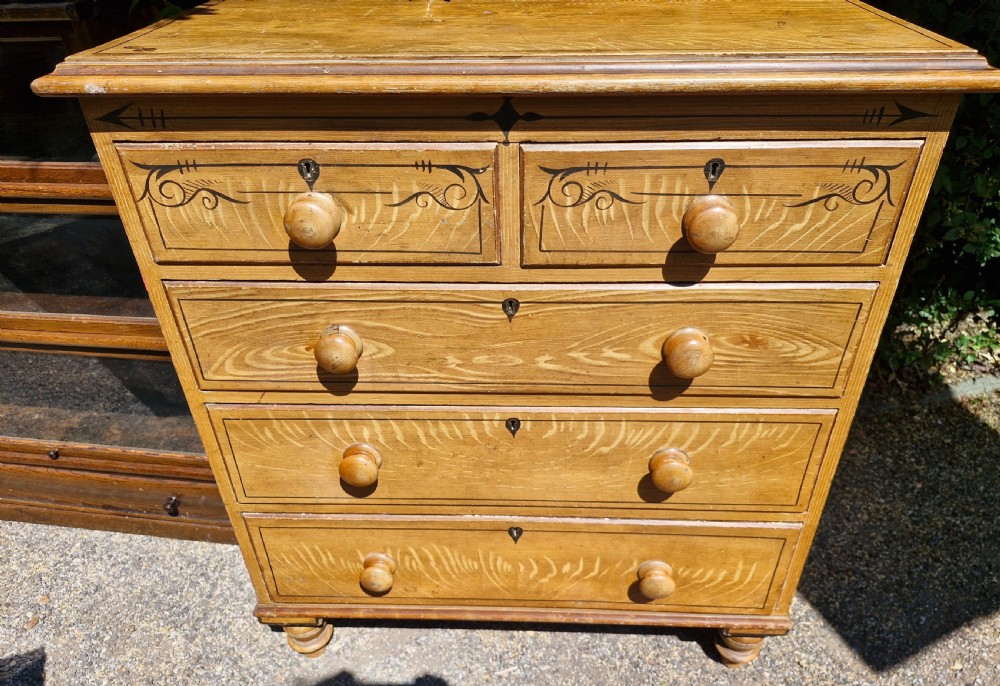 A Victorian scumbled pine chest of drawers featuring two short drawers over three long drawers with turned wooden handles and hand-painted decorative border detailing. View V