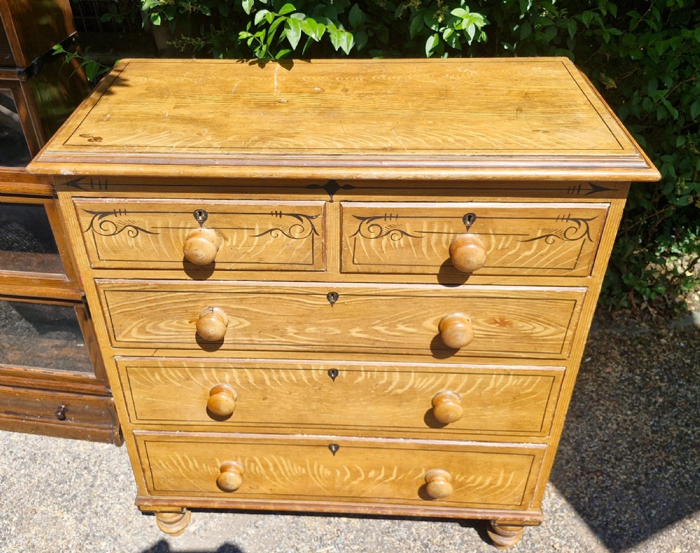 A Victorian scumbled pine chest of drawers featuring two short drawers over three long drawers with turned wooden handles and hand-painted decorative border detailing. View VI