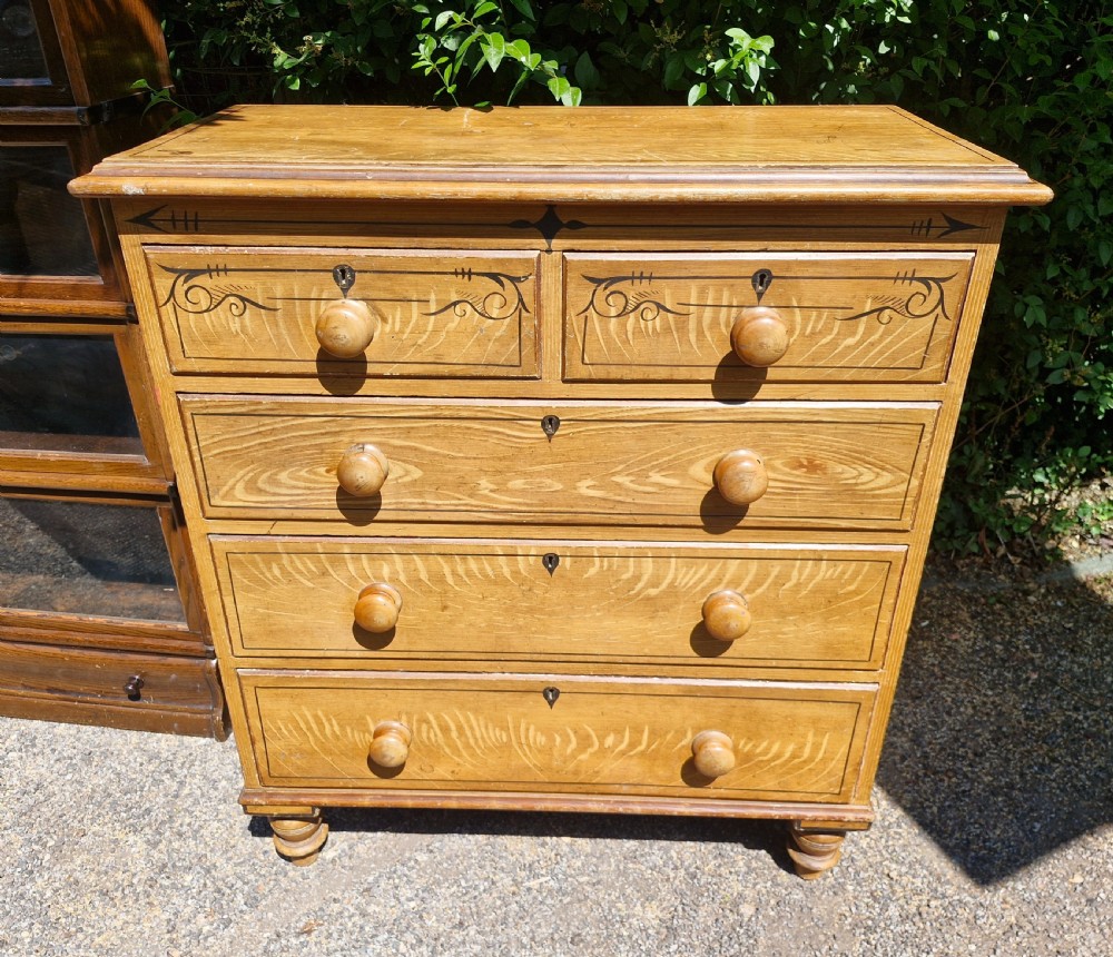 A Victorian scumbled pine chest of drawers featuring two short drawers over three long drawers with turned wooden handles and hand-painted decorative border detailing. View VII