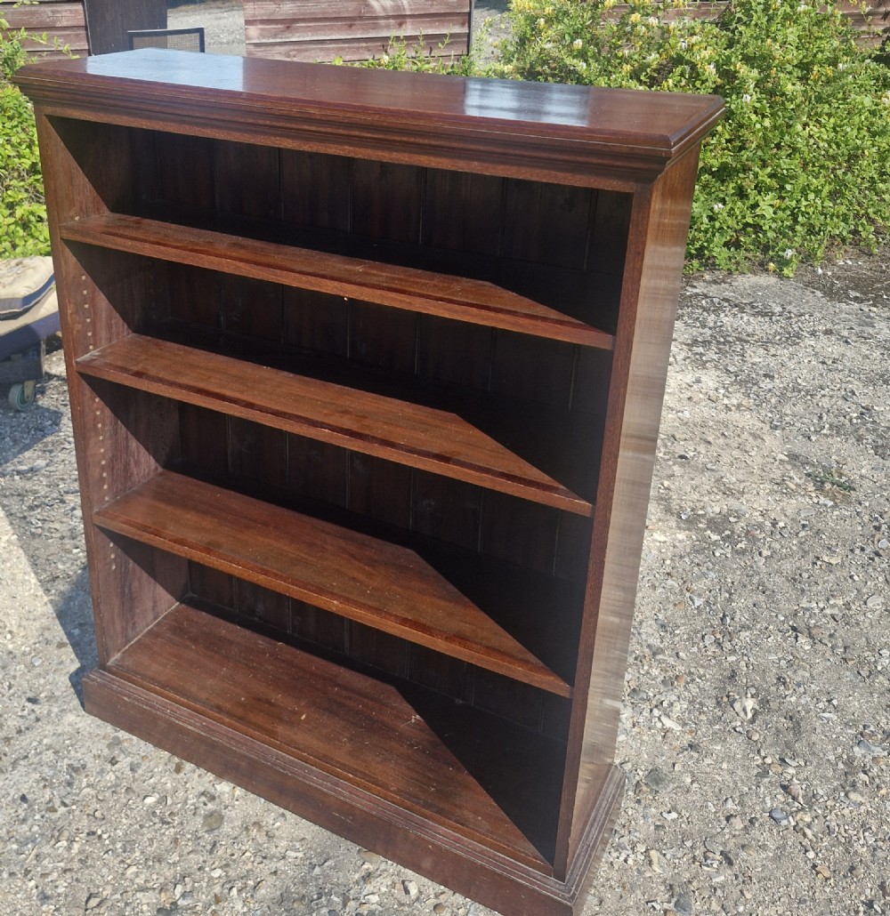 A low dark mahogany open front bookcase featuring four shelves, a moulded top, and a solid plinth base.