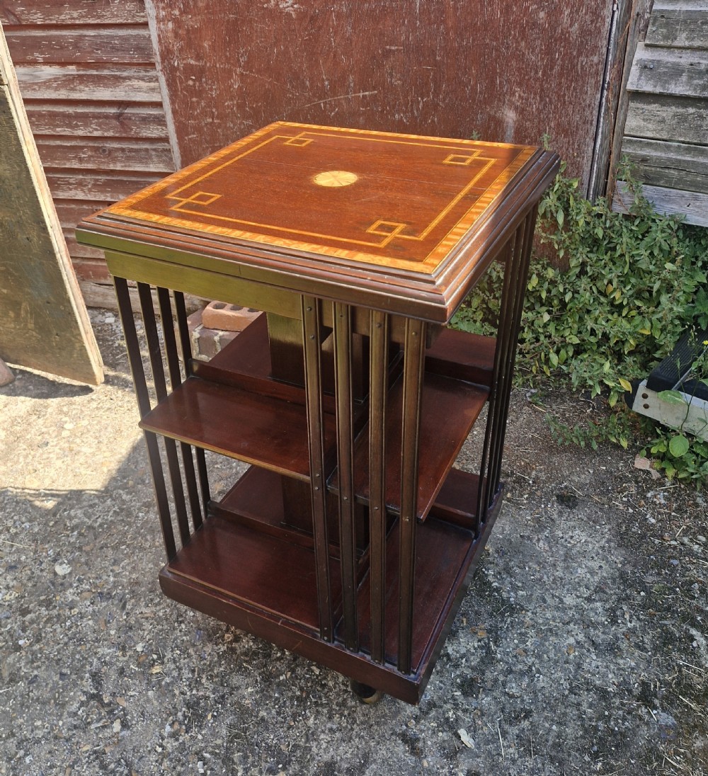 An Edwardian mahogany revolving bookcase featuring geometric satinwood inlay on the top surface, vertical slatted sides, and tiered shelves.
