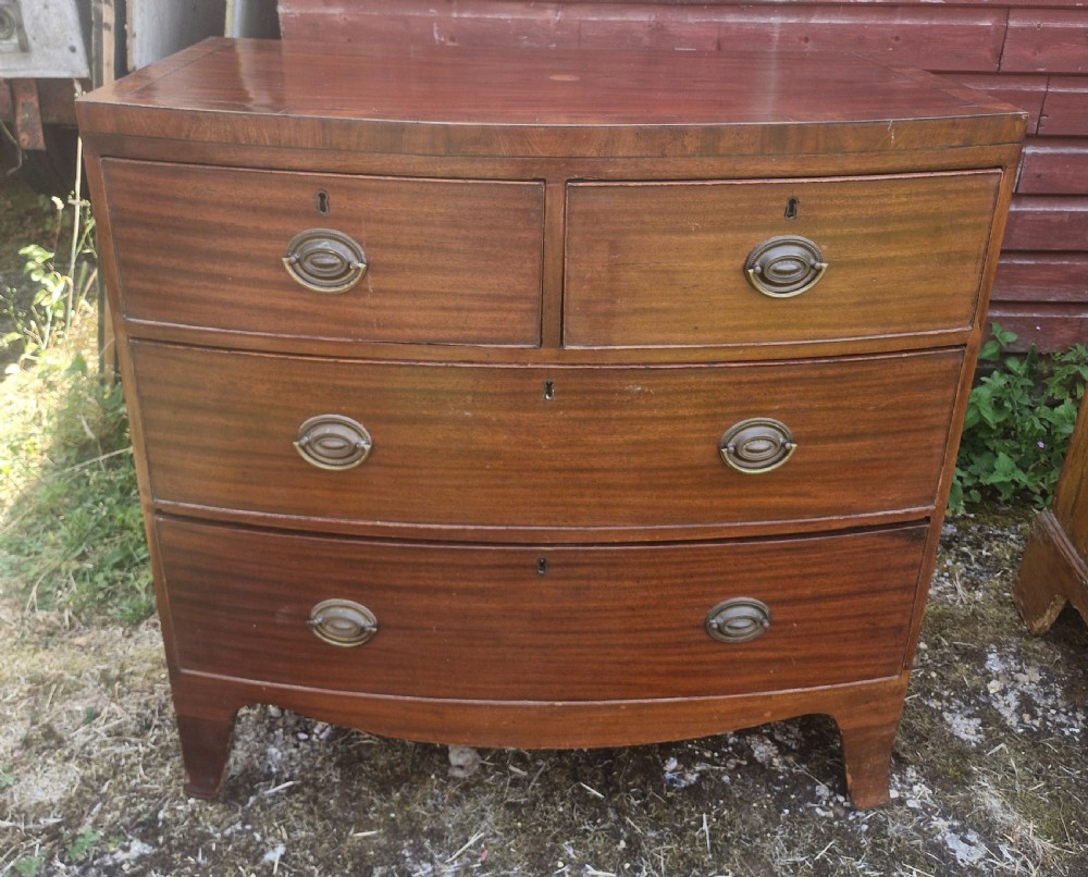 A Regency period mahogany bow front chest of drawers featuring two short drawers above two long drawers with oval brass handles and splayed feet.