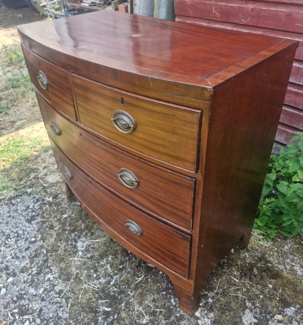 A Regency period mahogany bow front chest of drawers featuring two short drawers above two long drawers with oval brass handles and splayed feet. View II