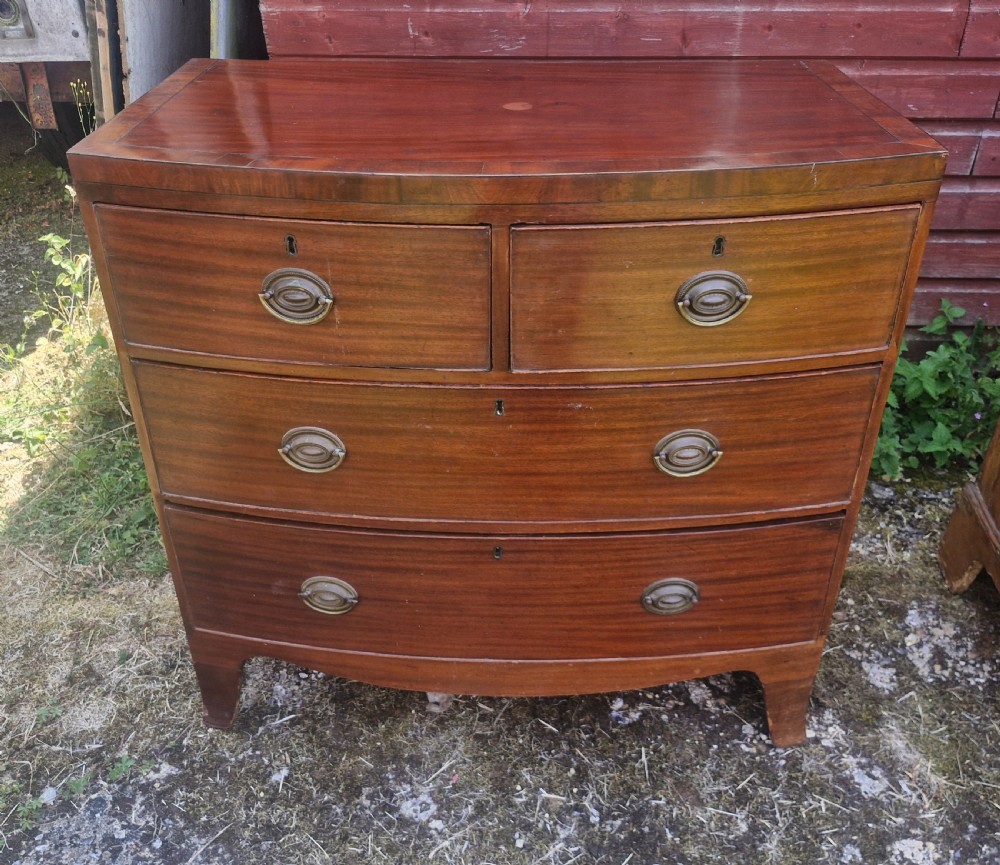 A Regency period mahogany bow front chest of drawers featuring two short drawers above two long drawers with oval brass handles and splayed feet. View III
