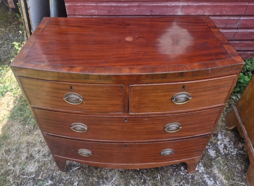 A Regency period mahogany bow front chest of drawers featuring two short drawers above two long drawers with oval brass handles and splayed feet. View IV