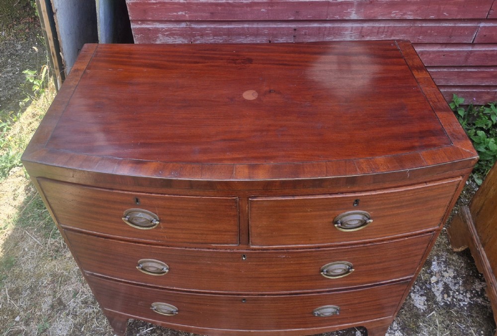 A Regency period mahogany bow front chest of drawers featuring two short drawers above two long drawers with oval brass handles and splayed feet. View VI