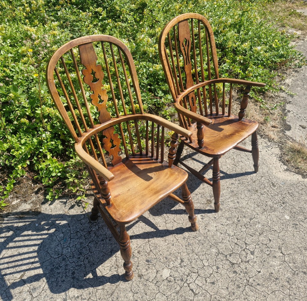 A matched pair of warm brown wooden Windsor armchairs featuring hoop backs, pierced central splats, turned spindles, and shaped solid seats.