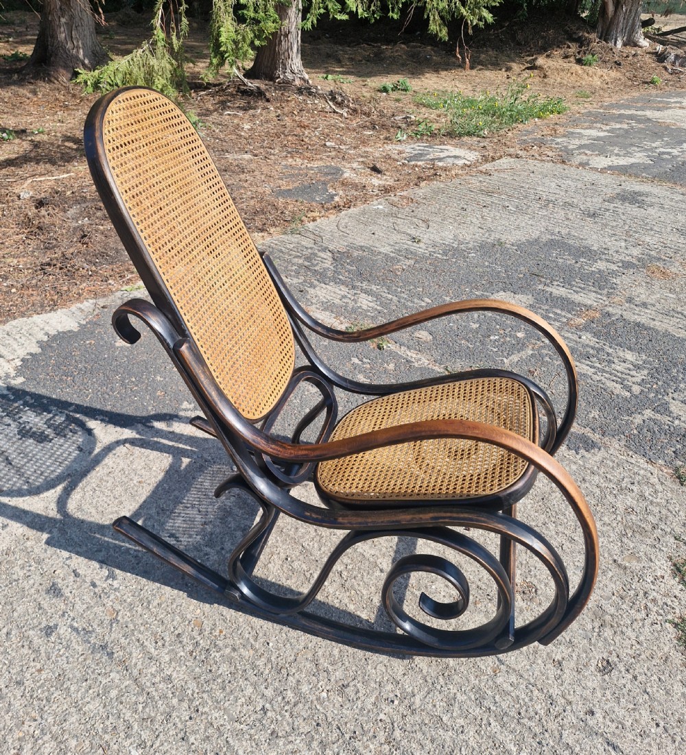A dark brown bentwood rocking armchair featuring prominent scrollwork side frames with woven rattan cane backrest and seat panels.