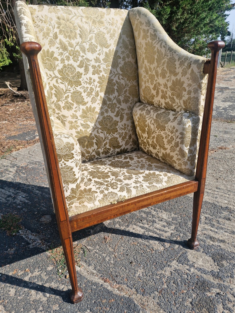 An Art Nouveau mahogany armchair featuring a high back, gold floral damask upholstery, boxwood inlay stringing, and extended vertical side supports ending in rounded finials.
