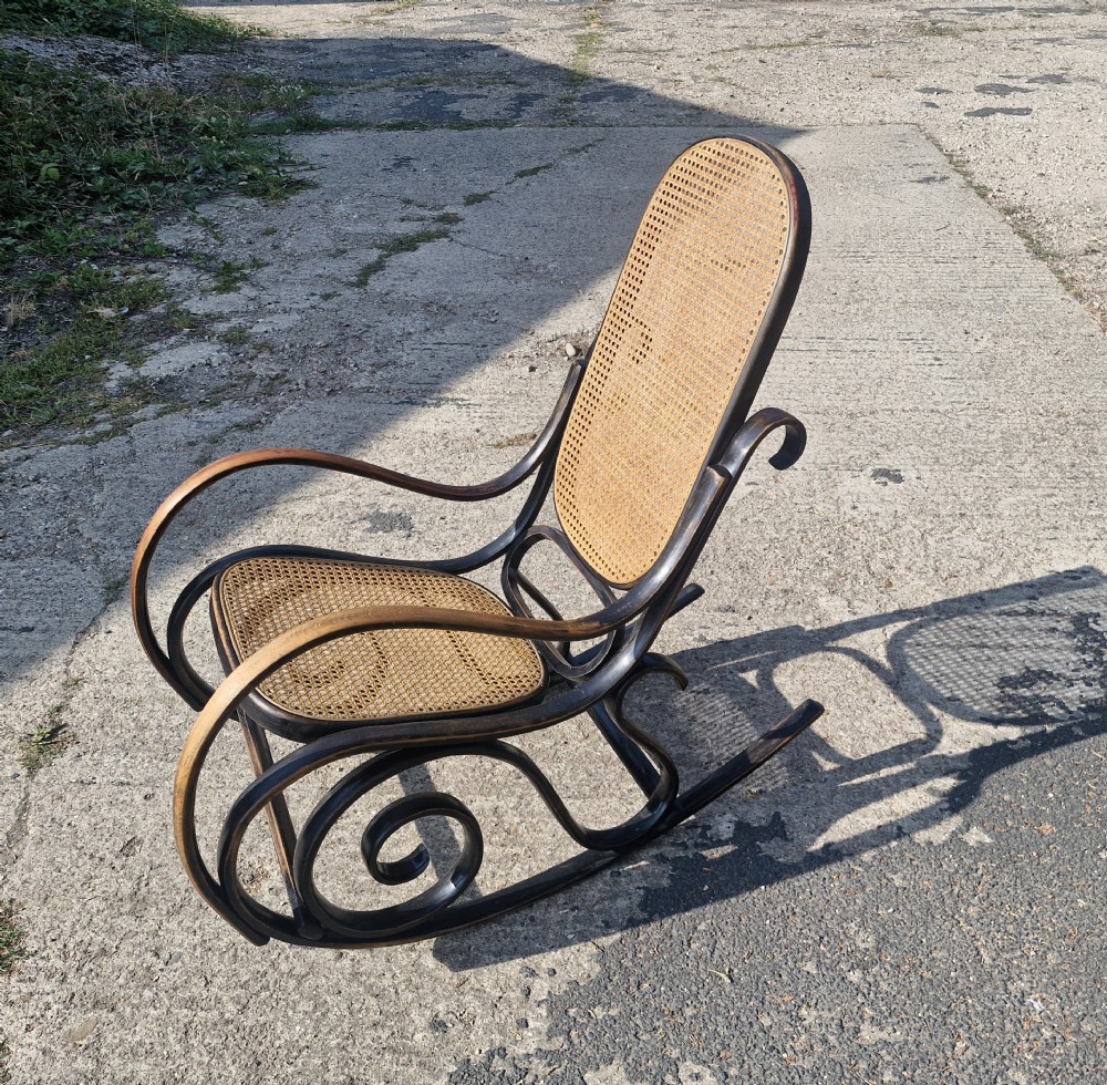 A dark brown bentwood rocking armchair featuring prominent scrollwork side frames with woven rattan cane backrest and seat panels. View III