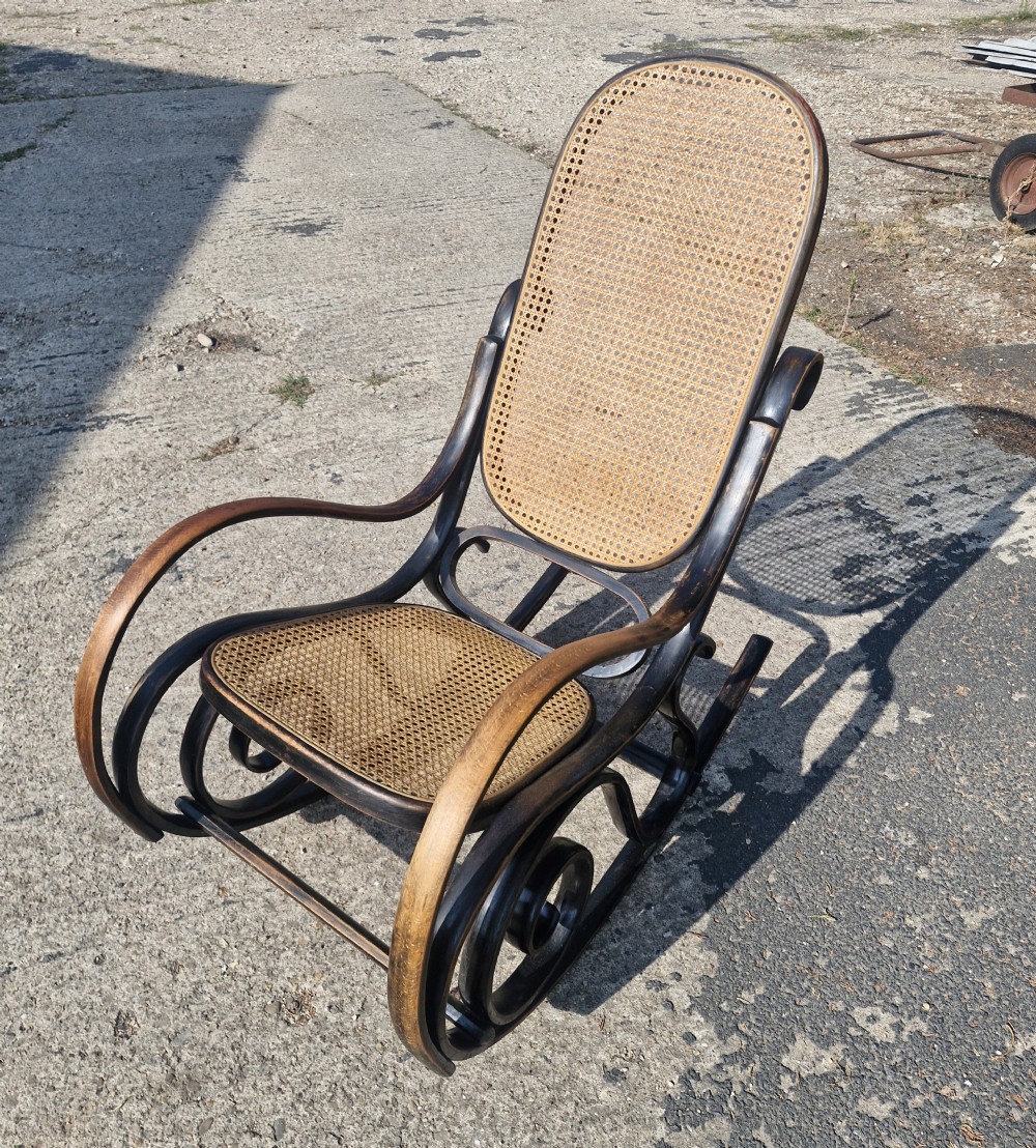 A dark brown bentwood rocking armchair featuring prominent scrollwork side frames with woven rattan cane backrest and seat panels. View VI