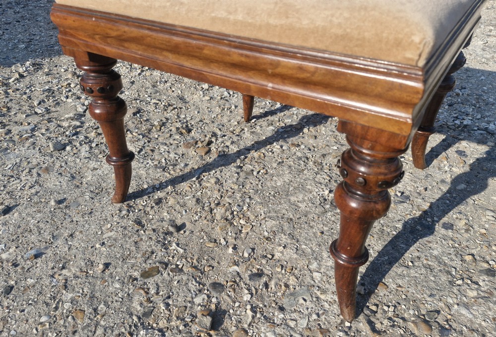 A square Victorian footstool featuring turned wooden legs and a beige upholstered padded top. View II