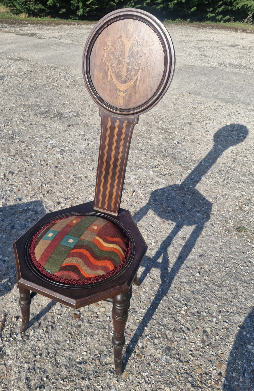 An Edwardian dark wood spinning chair featuring a tall narrow backrest with marquetry inlay and an upholstered circular seat within a hexagonal frame.