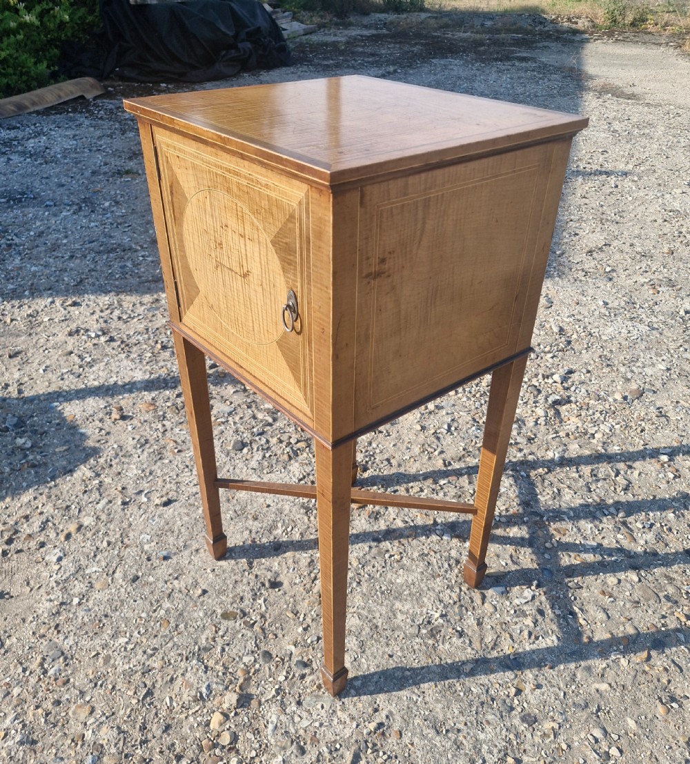 An Edwardian satinwood bedside cabinet featuring fine line stringing, an oval inlay design on the single door, square tapered legs, and an X-frame stretcher. View IV