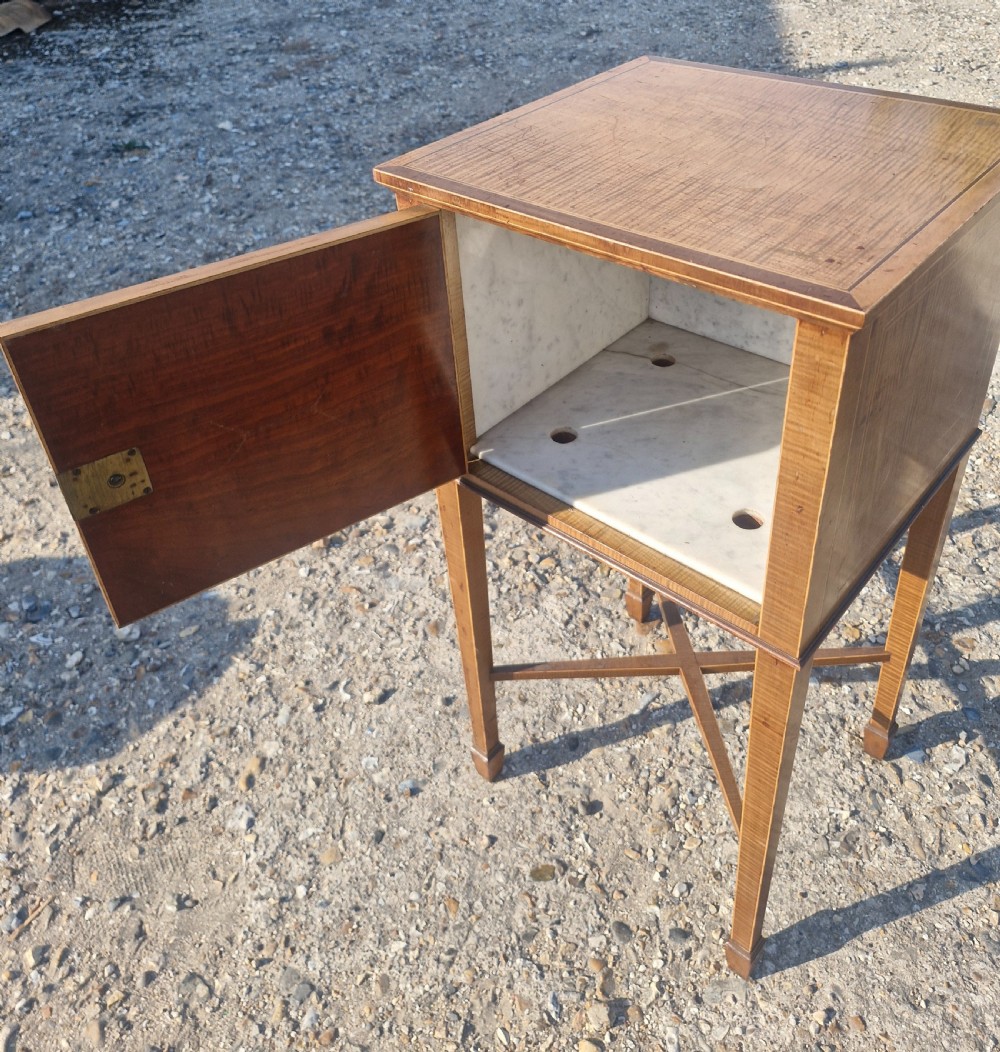 An Edwardian satinwood bedside cabinet featuring fine line stringing, an oval inlay design on the single door, square tapered legs, and an X-frame stretcher. View VI