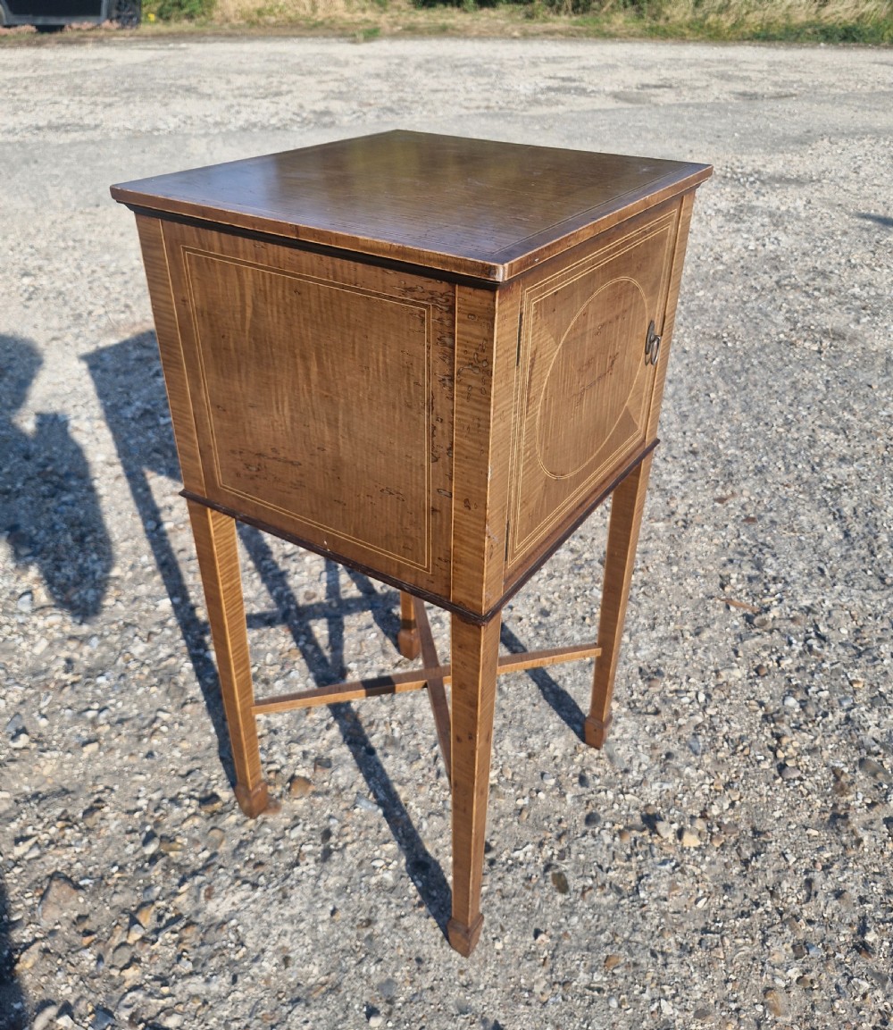 An Edwardian satinwood bedside cabinet featuring fine line stringing, an oval inlay design on the single door, square tapered legs, and an X-frame stretcher. View VII
