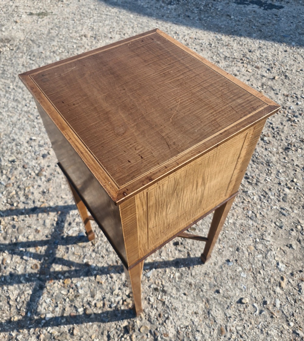 An Edwardian satinwood bedside cabinet featuring fine line stringing, an oval inlay design on the single door, square tapered legs, and an X-frame stretcher. View VIII