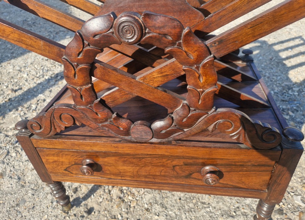 A Regency rosewood Canterbury featuring slatted division compartments, central carved leaf wreath motifs, a base drawer with turned handles, and turned legs on brass castors. View VII
