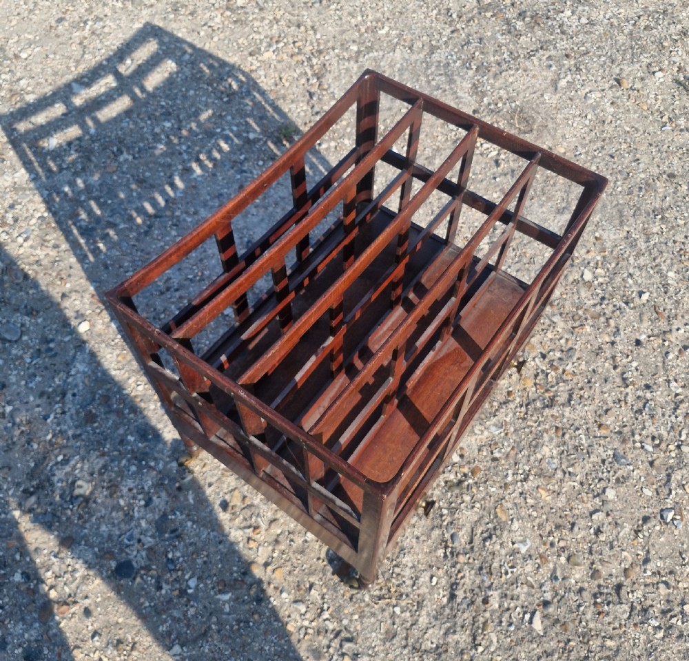 A 19th century mahogany Canterbury with slatted vertical divisions, a lower base drawer with brass knobs, and turned legs with brass castors. View V