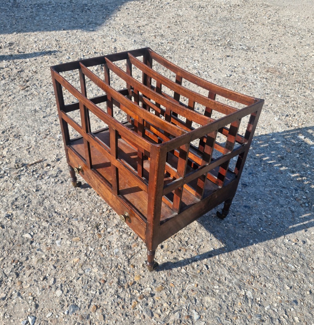 A 19th century mahogany Canterbury with slatted vertical divisions, a lower base drawer with brass knobs, and turned legs with brass castors. View VI