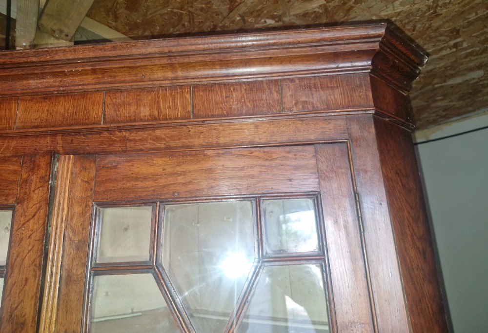 An antique two-part Welsh oak corner cupboard featuring upper astragal glazed doors with geometric panes and lower panelled cupboard doors. View V