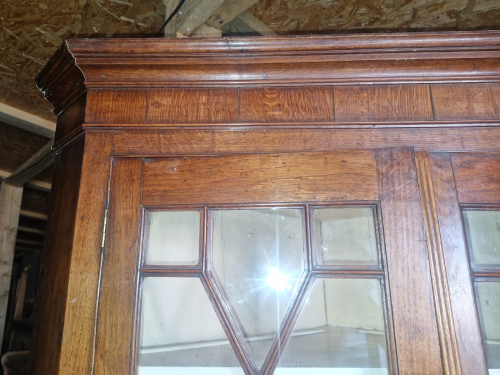 An antique two-part Welsh oak corner cupboard featuring upper astragal glazed doors with geometric panes and lower panelled cupboard doors. View VI