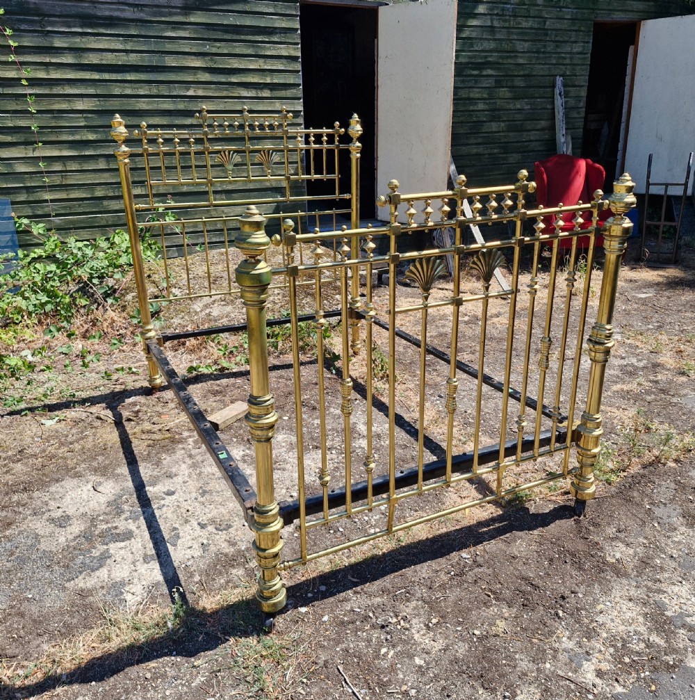 A Victorian double brass bed frame featuring turned posts, decorative finials, vertical metal spindles, and cast iron side rails.
