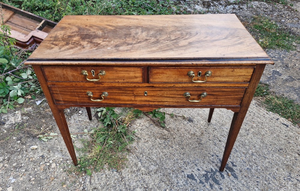 An early 19th-century mahogany side table featuring a rectangular top, three drawers with brass handles, and slender square tapered legs.