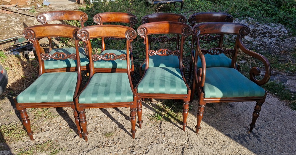 A set of eight Regency mahogany dining chairs featuring scroll-carved crest rails, decorative central splats, green striped fabric seats, and turned front legs.