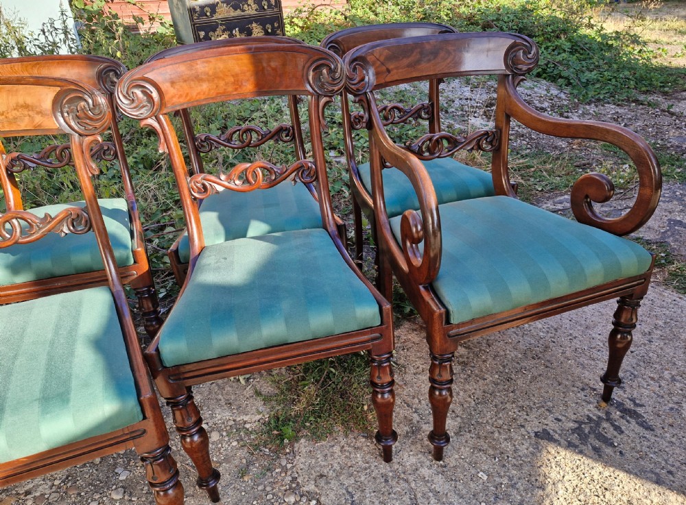 A set of eight Regency mahogany dining chairs featuring scroll-carved crest rails, decorative central splats, green striped fabric seats, and turned front legs. View II
