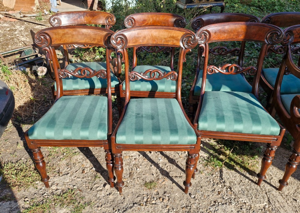 A set of eight Regency mahogany dining chairs featuring scroll-carved crest rails, decorative central splats, green striped fabric seats, and turned front legs. View IV