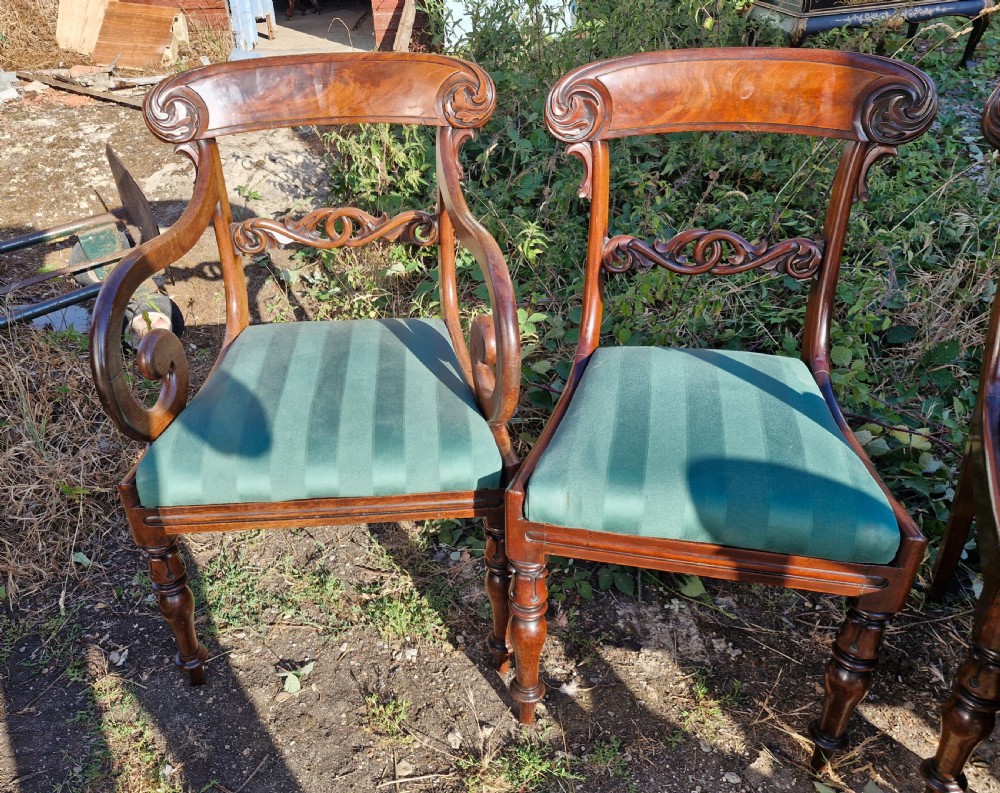 A set of eight Regency mahogany dining chairs featuring scroll-carved crest rails, decorative central splats, green striped fabric seats, and turned front legs. View V