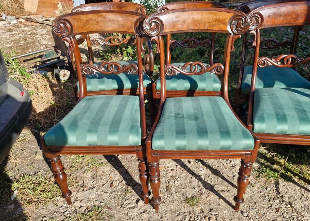 A set of eight Regency mahogany dining chairs featuring scroll-carved crest rails, decorative central splats, green striped fabric seats, and turned front legs. View VI